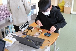 マイクロビットを組み入れた回路で豆電球を点灯させる児童の写真