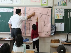 大きな地図で建物の位置を確認する教師と児童の写真