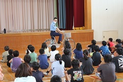 体育館で自転車の乗り方の話を聞く児童の写真