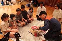 AEDの説明を聞く児童と保護者の写真