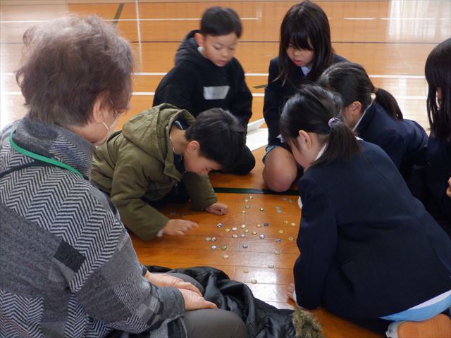 地域ボランティアさんに見守られておはじきに挑戦する児童