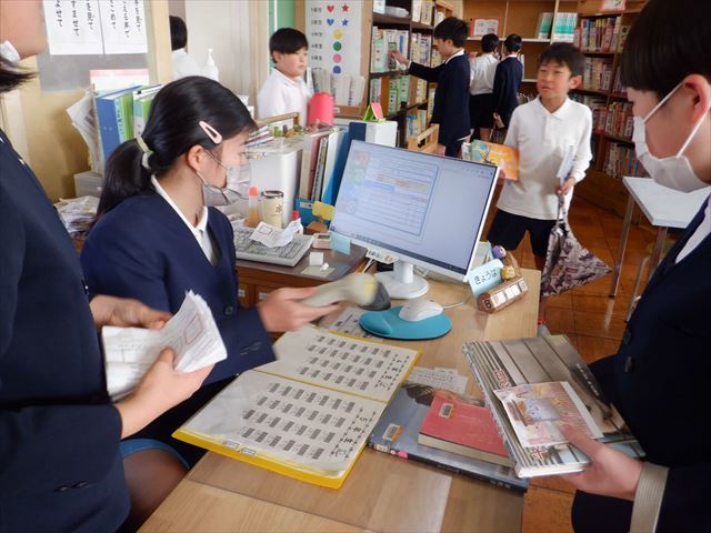 図書館キャラクターが挟んである本を見つけ、図書当番に手続きをしてもらう児童