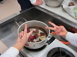 芋を蒸す鍋の上でピースする児童の写真